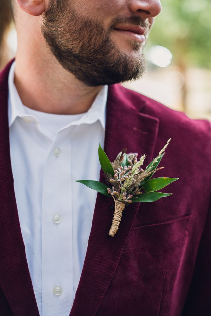 mountain-wedding-circle-arch-web-4 groom wearing maroon velvet jacket with boutonniere of feathers and greenery