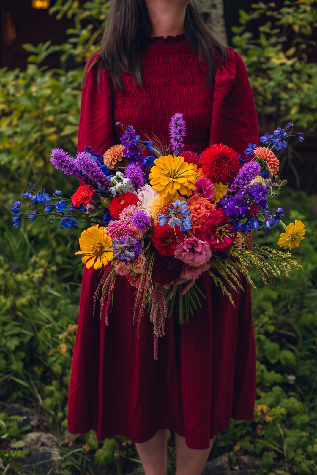 wild-blossoms-rocky-mountain-colorful-circle-arch-wedding-web-4 woman in red dress holding a vibrant jewel tone bouquet of summer wedding flowers in estes park colorado